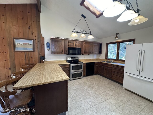 kitchen with light tile patterned flooring, dark brown cabinets, black appliances, wood walls, and vaulted ceiling with skylight