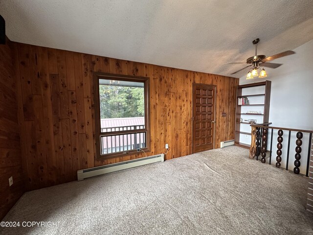 unfurnished room with ceiling fan, wooden walls, a baseboard radiator, carpet, and a textured ceiling