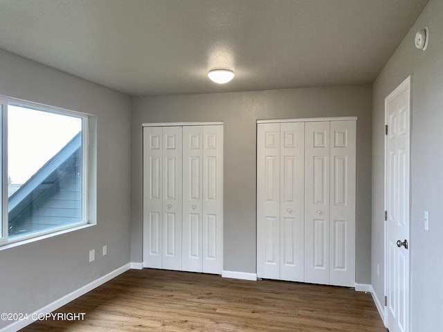 unfurnished bedroom featuring hardwood / wood-style floors and two closets