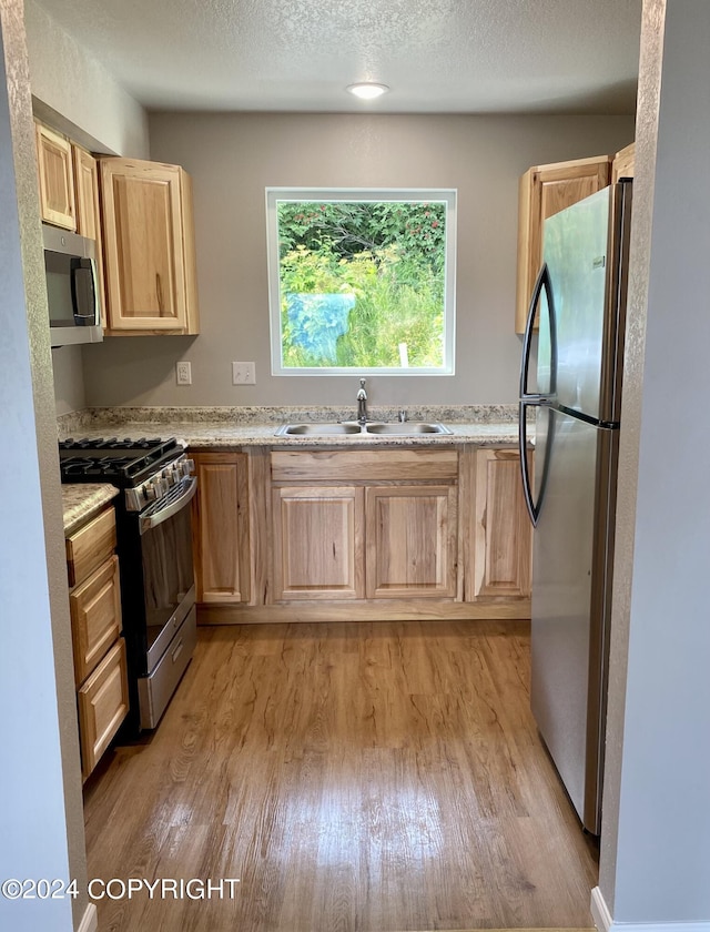 kitchen with light brown cabinetry, sink, light hardwood / wood-style floors, stainless steel appliances, and a textured ceiling