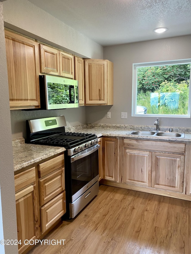 kitchen with sink, stainless steel appliances, light stone countertops, a textured ceiling, and light hardwood / wood-style flooring