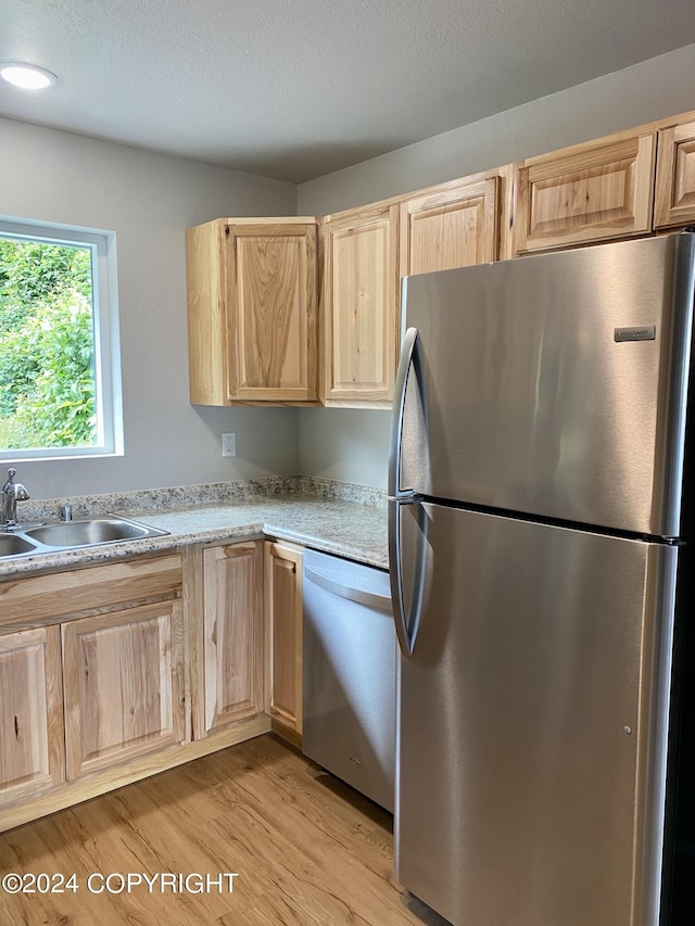 kitchen with appliances with stainless steel finishes, sink, light wood-type flooring, light brown cabinets, and a textured ceiling