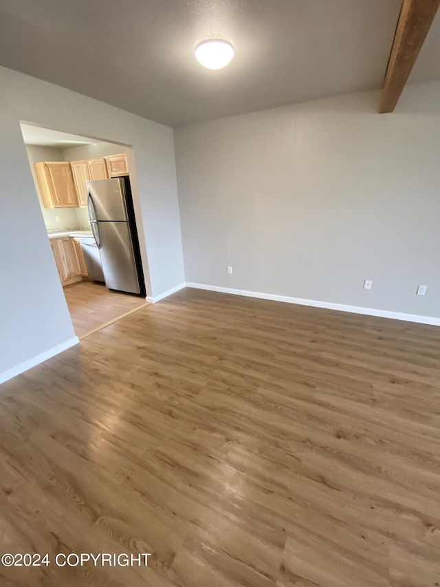 empty room featuring beam ceiling and light hardwood / wood-style floors