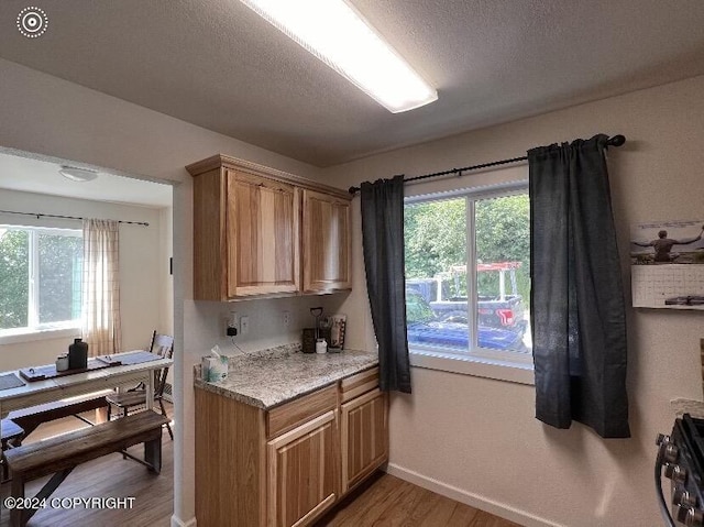 kitchen with light stone counters, light hardwood / wood-style flooring, stove, and a textured ceiling