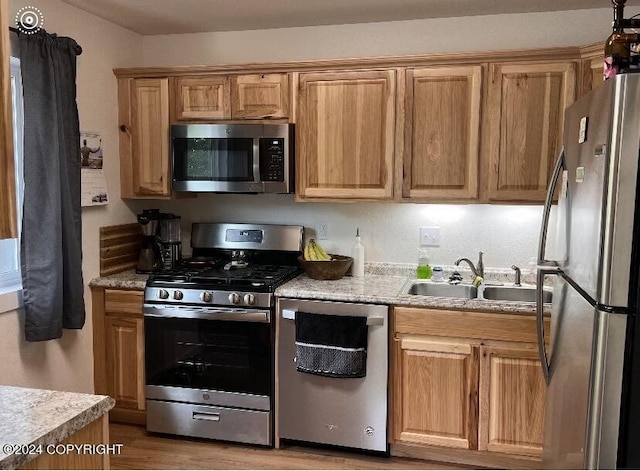 kitchen with sink, stainless steel appliances, light stone countertops, and light wood-type flooring