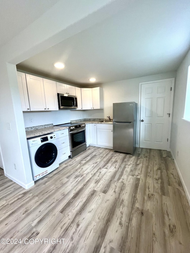 kitchen featuring appliances with stainless steel finishes, white cabinetry, washer / dryer, sink, and light hardwood / wood-style floors