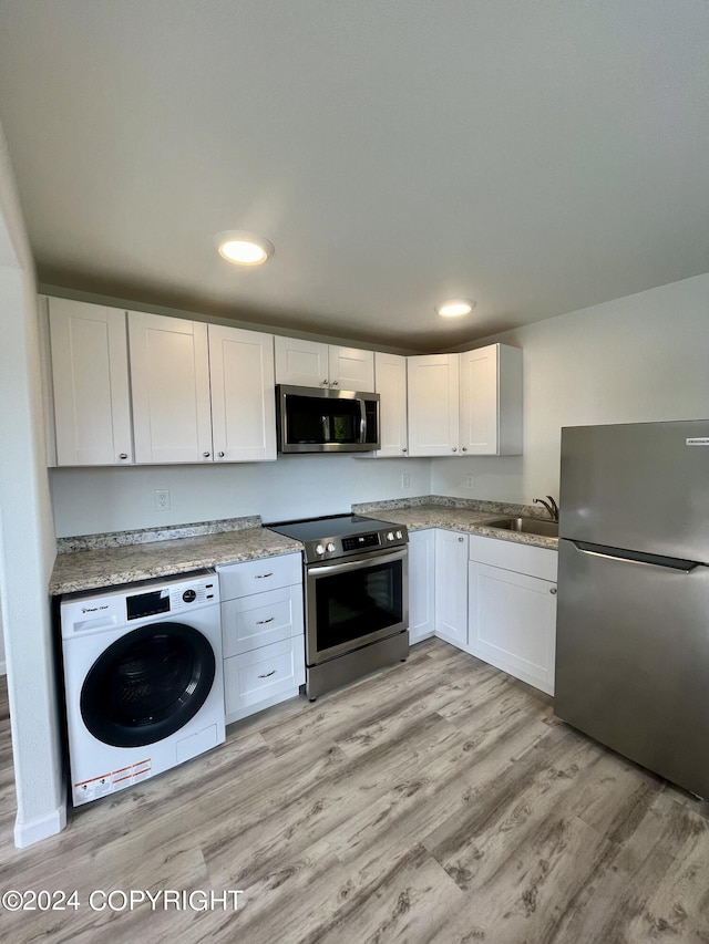 kitchen with washer / dryer, sink, white cabinetry, appliances with stainless steel finishes, and light hardwood / wood-style floors