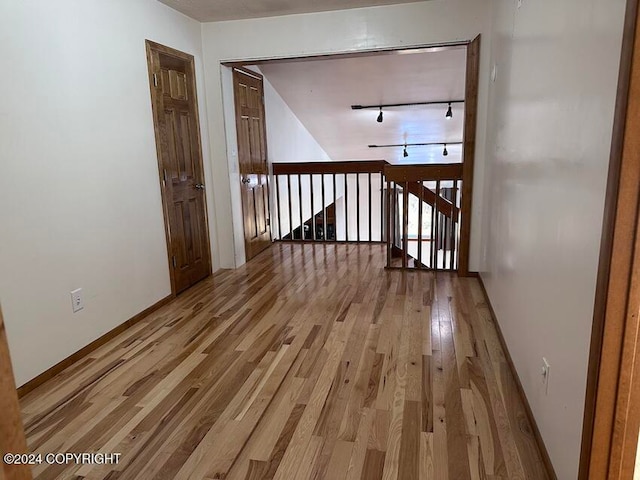 corridor with rail lighting and light hardwood / wood-style floors