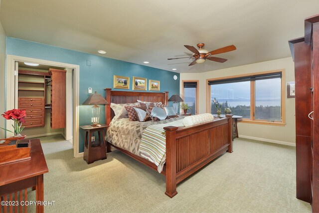 bedroom featuring a walk in closet, light colored carpet, and ceiling fan