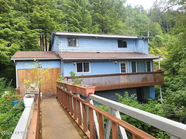 view of front of home with a deck, a shingled roof, and a view of trees