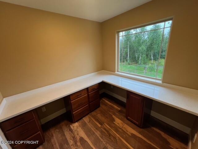 unfurnished office featuring built in desk and dark hardwood / wood-style flooring