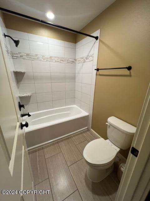 bathroom with tiled shower / bath combo, toilet, and tile patterned flooring