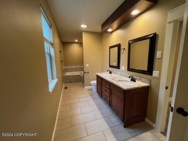 bathroom featuring tile patterned flooring, tiled bath, toilet, and double sink vanity