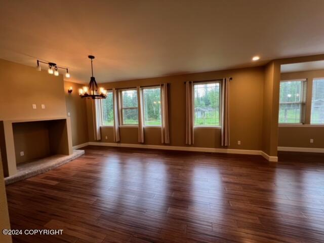 unfurnished living room featuring dark hardwood / wood-style flooring, rail lighting, and an inviting chandelier