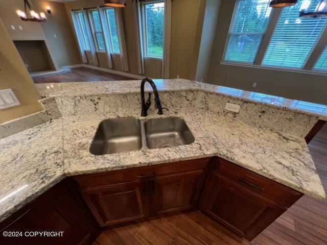 kitchen with sink, pendant lighting, light stone countertops, and hardwood / wood-style flooring