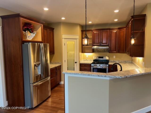 kitchen with decorative light fixtures, hardwood / wood-style floors, light stone counters, appliances with stainless steel finishes, and kitchen peninsula