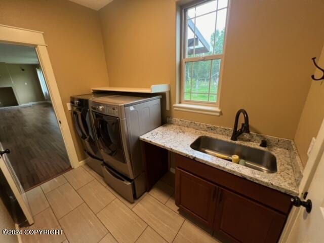 clothes washing area featuring sink, light hardwood / wood-style flooring, washer and dryer, and a wealth of natural light