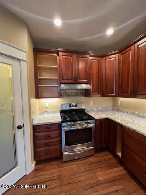 kitchen with stainless steel range with gas stovetop, range hood, light stone counters, and dark wood-type flooring