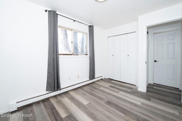 unfurnished bedroom featuring hardwood / wood-style flooring, a closet, and a baseboard heating unit