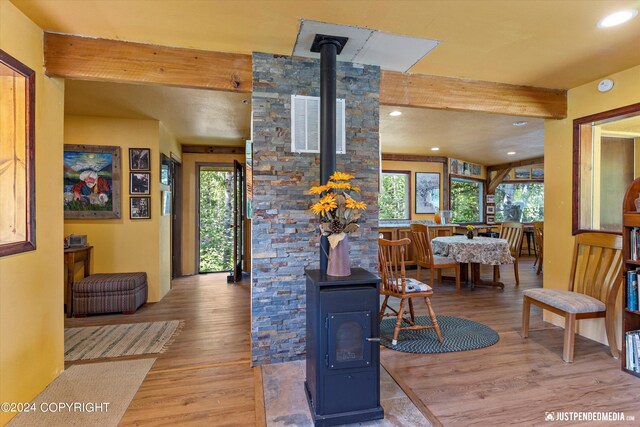 living room with hardwood / wood-style flooring, beam ceiling, a wood stove, and plenty of natural light