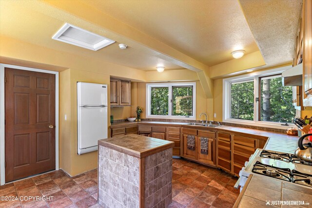 kitchen with a textured ceiling, tile countertops, sink, and white appliances