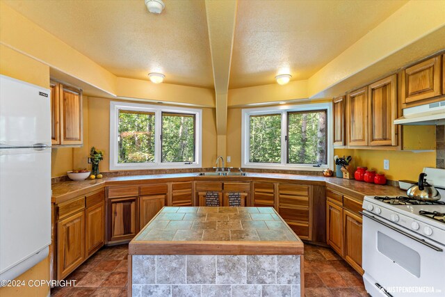 kitchen featuring a textured ceiling, sink, white appliances, and a center island