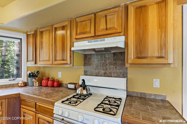 kitchen with backsplash, white gas range oven, and tile countertops