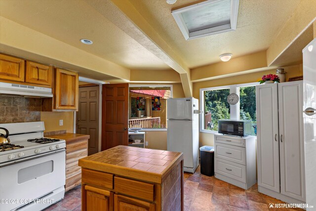 kitchen with a textured ceiling, white appliances, tasteful backsplash, and tile countertops