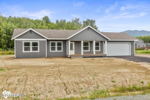 ranch-style house featuring a garage, driveway, roof with shingles, and a mountain view