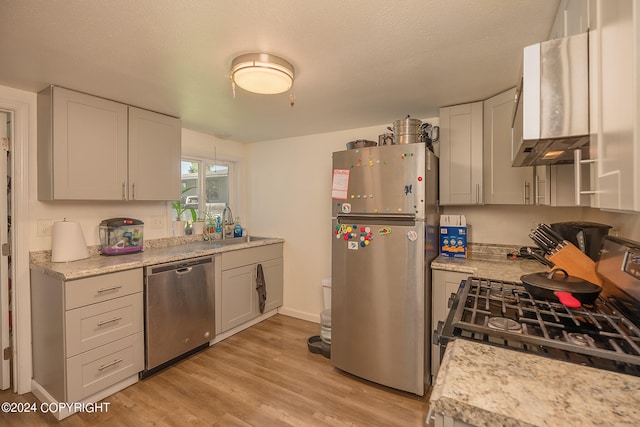 kitchen featuring appliances with stainless steel finishes, light hardwood / wood-style flooring, sink, a textured ceiling, and wall chimney range hood