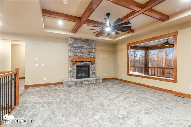 unfurnished living room featuring a stone fireplace, carpet, coffered ceiling, beam ceiling, and ceiling fan