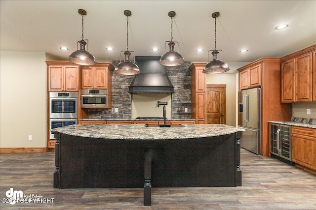 kitchen featuring an island with sink, stainless steel appliances, hardwood / wood-style flooring, and custom range hood