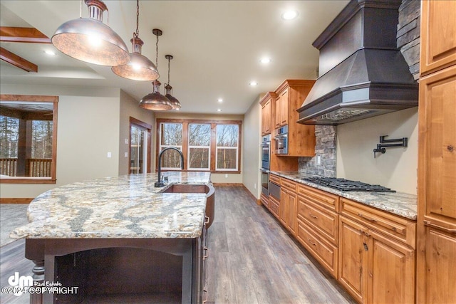 kitchen with a kitchen island with sink, custom exhaust hood, sink, dark wood-type flooring, and stainless steel gas cooktop