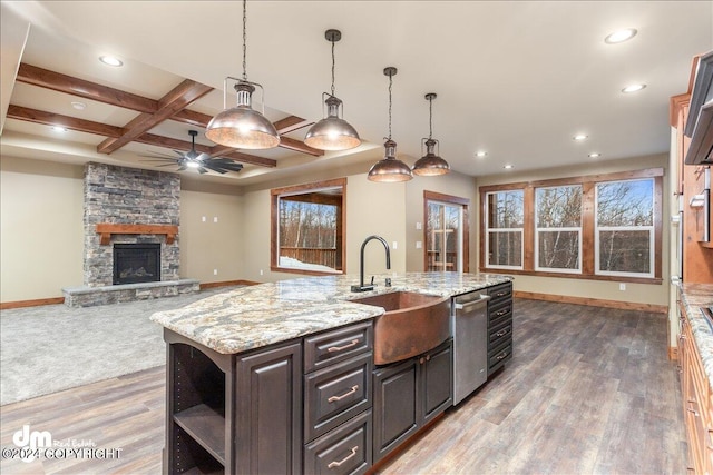 kitchen with hardwood / wood-style floors, dishwasher, a fireplace, a center island with sink, and sink