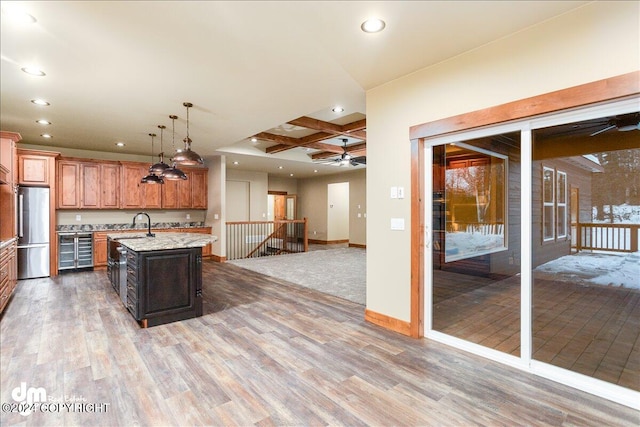 kitchen with an island with sink, coffered ceiling, hardwood / wood-style floors, and ceiling fan