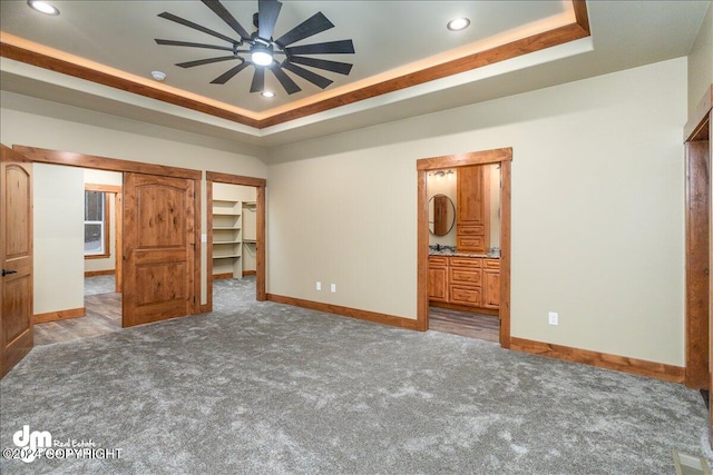 unfurnished bedroom featuring a walk in closet, a tray ceiling, ceiling fan, and carpet floors