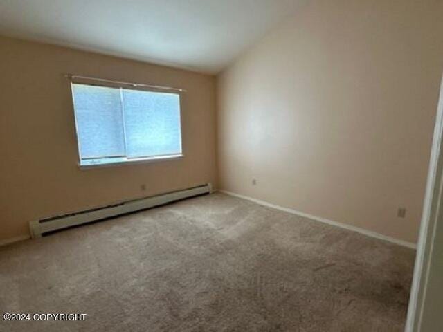 carpeted spare room with a baseboard radiator, vaulted ceiling, and baseboards