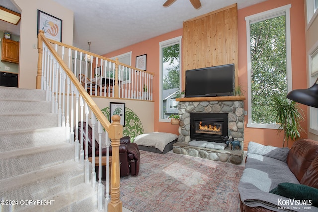 living room featuring a textured ceiling, plenty of natural light, ceiling fan, and a stone fireplace