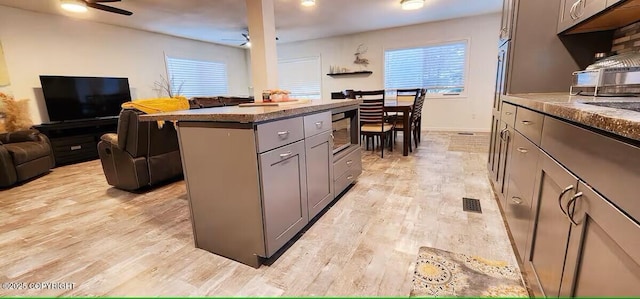 kitchen featuring ceiling fan, a kitchen island, gray cabinetry, and light hardwood / wood-style flooring