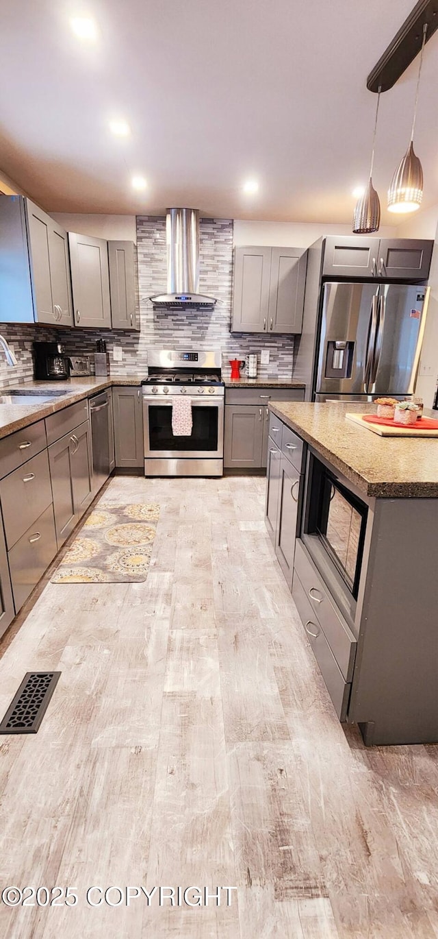 kitchen featuring stainless steel appliances, wall chimney range hood, decorative light fixtures, gray cabinets, and sink