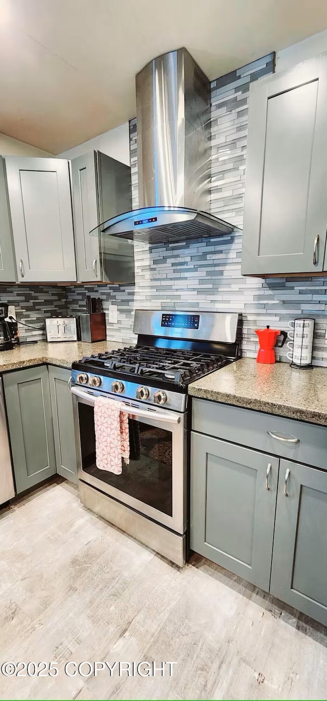 kitchen with gas range, tasteful backsplash, wall chimney range hood, and light stone counters