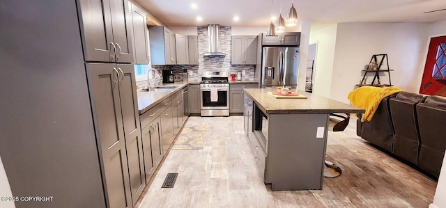 kitchen featuring appliances with stainless steel finishes, a center island, pendant lighting, wall chimney range hood, and a breakfast bar area