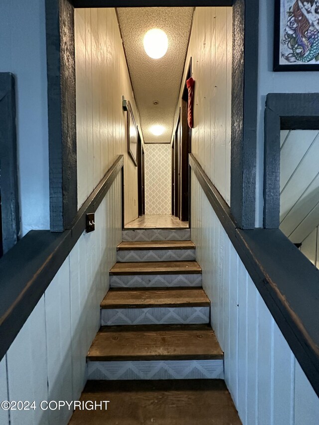 stairs featuring a textured ceiling and wooden walls