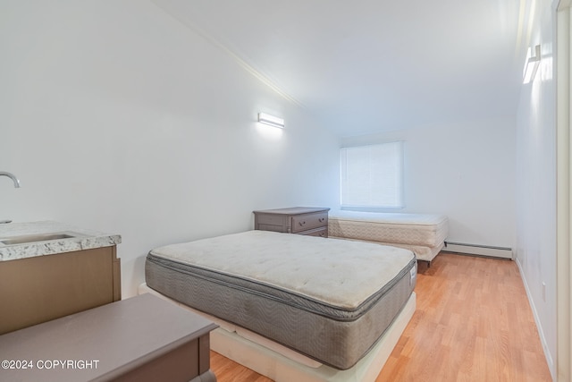 bedroom with a baseboard radiator, lofted ceiling, sink, and light wood-type flooring