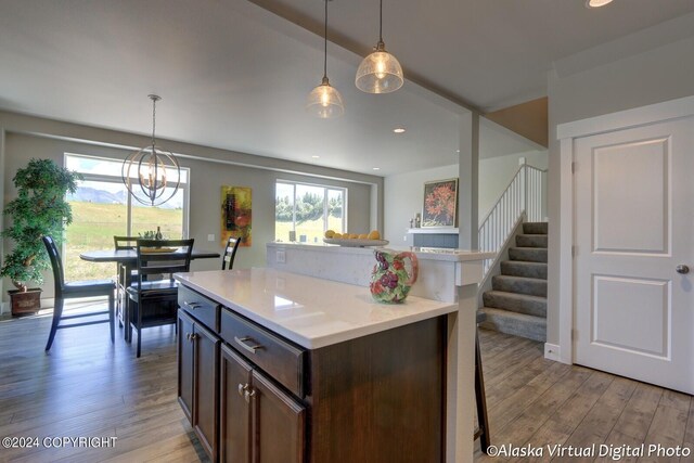 kitchen with light wood-type flooring, dark brown cabinetry, pendant lighting, and light stone countertops