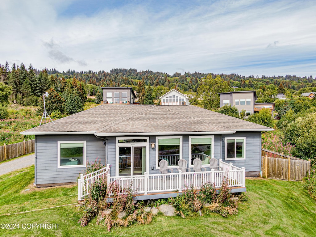 view of front facade featuring a front lawn, fence, a wooden deck, and a view of trees