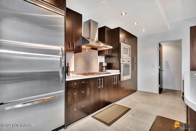 kitchen featuring tasteful backsplash, dark brown cabinetry, wall chimney range hood, and built in appliances