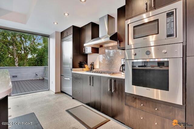 kitchen with built in appliances, dark brown cabinetry, recessed lighting, wall chimney range hood, and decorative backsplash