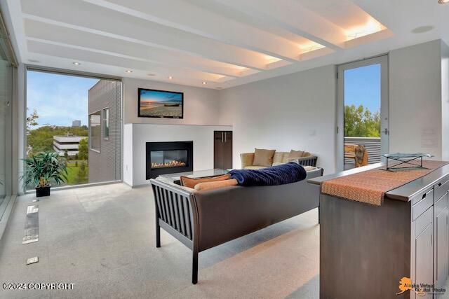 living area featuring beamed ceiling and a glass covered fireplace