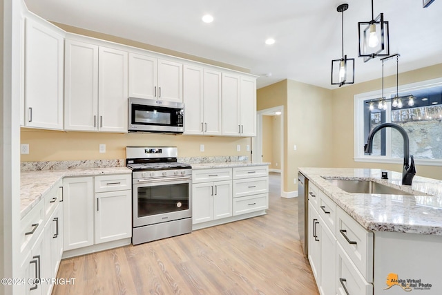 kitchen featuring sink, white cabinetry, hanging light fixtures, light hardwood / wood-style flooring, and appliances with stainless steel finishes